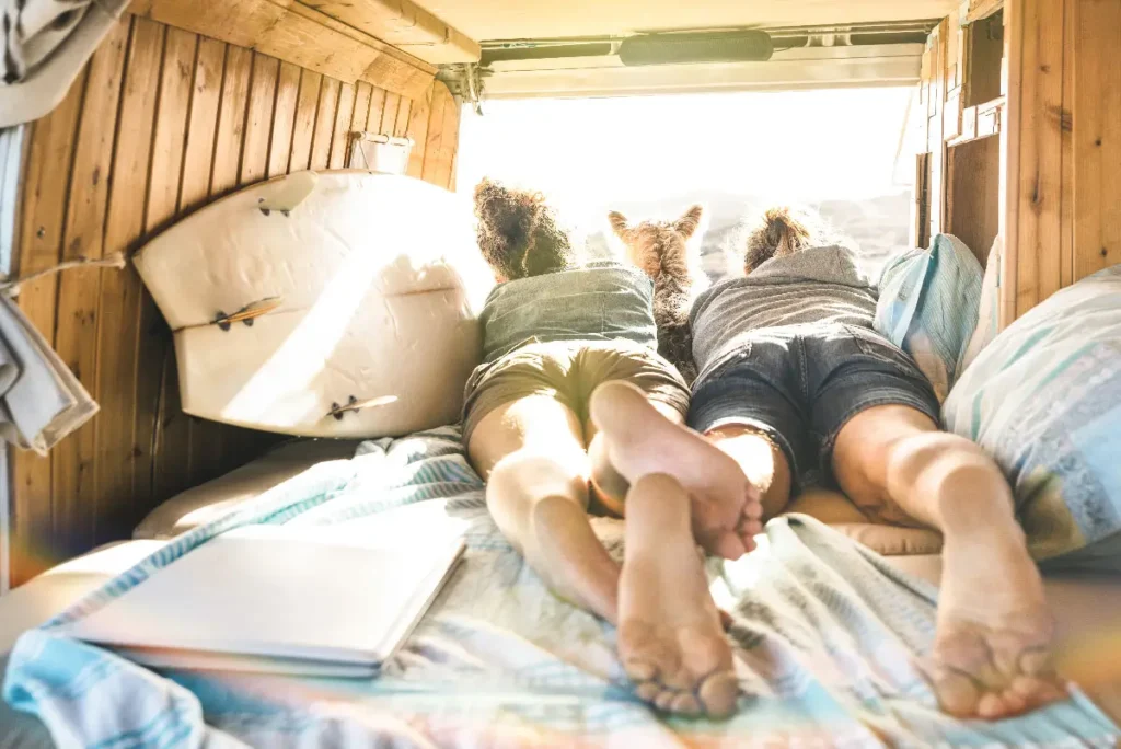 Young couple and dog relaxing in a camper van interior with cozy bedding and surfboard storage - B&S RV Supply.
